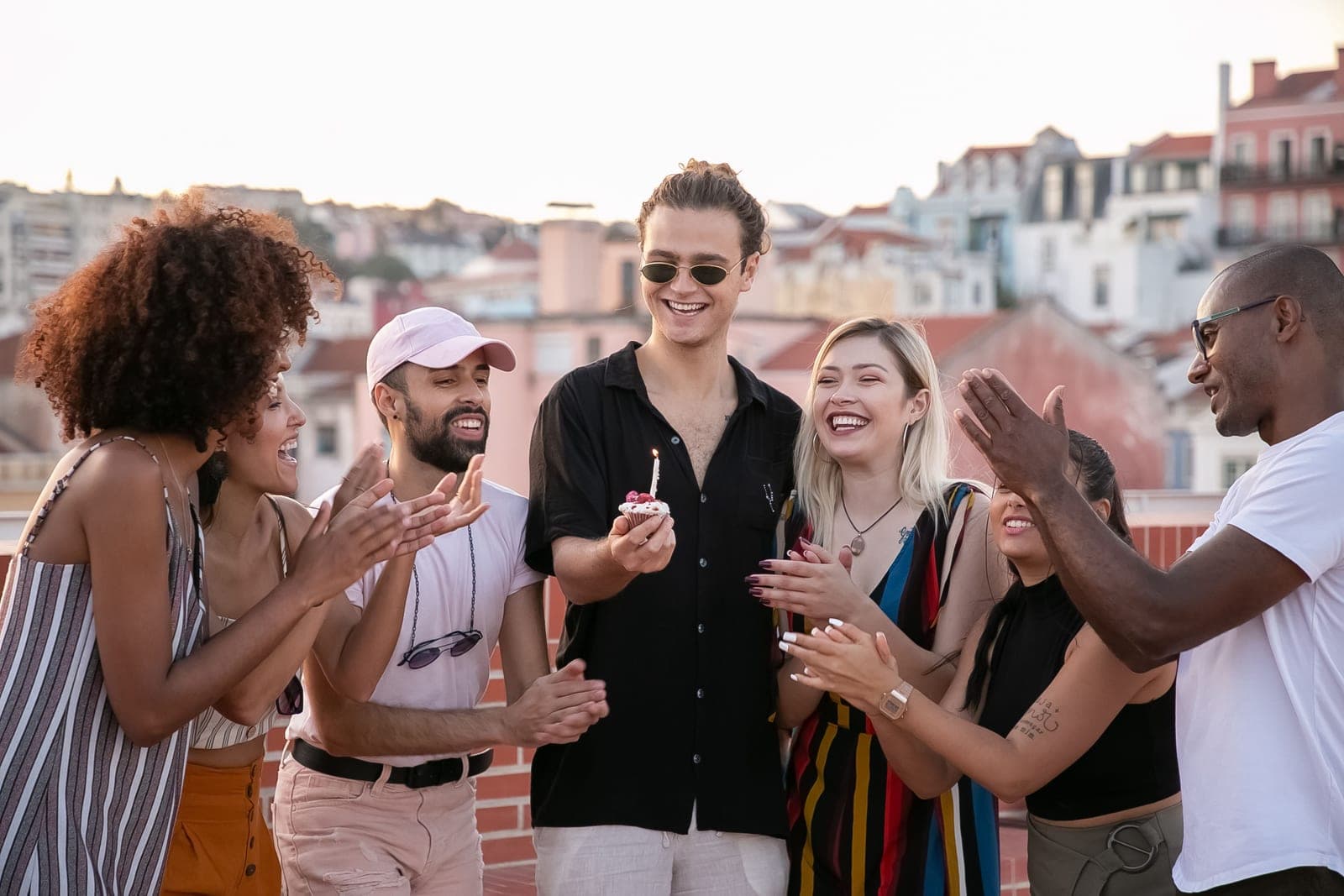 Friends on a rooftop applauding as a man holds a cupcake with a lit candle