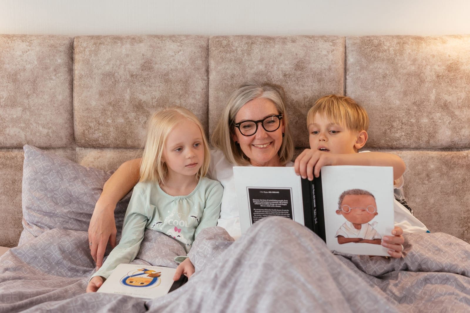 A grandmother reading picture books in bed with two young children