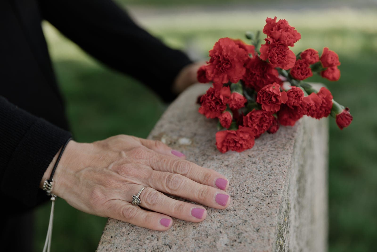 A hand resting on a headstone beside a bunch of red carnations