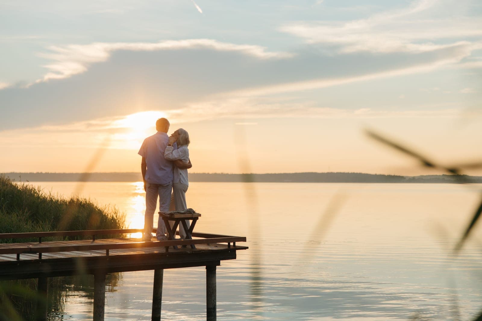 An older couple embracing at the end of a jetty at sunset