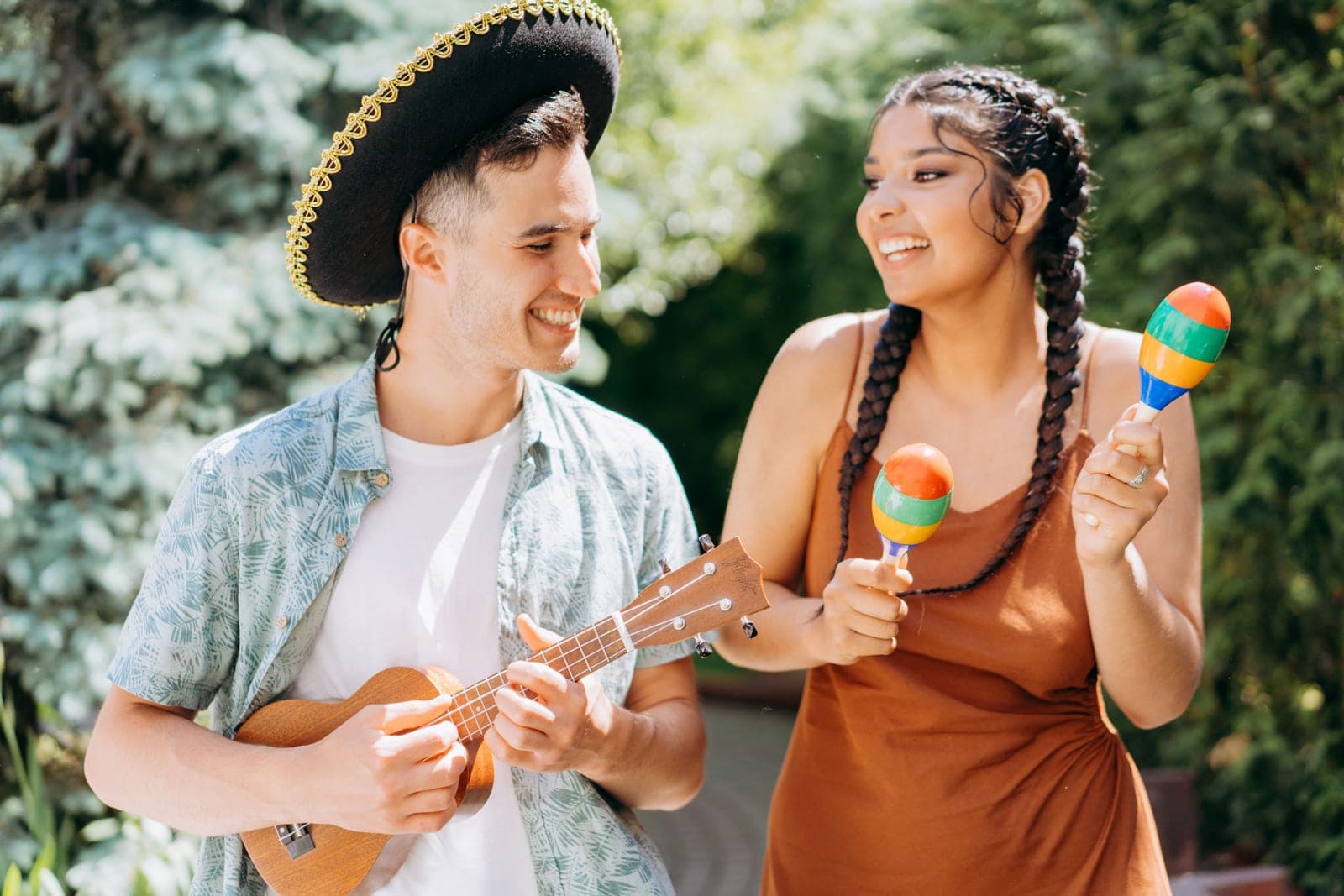 A couple outdoors playing a ukulele and maracas, laughing