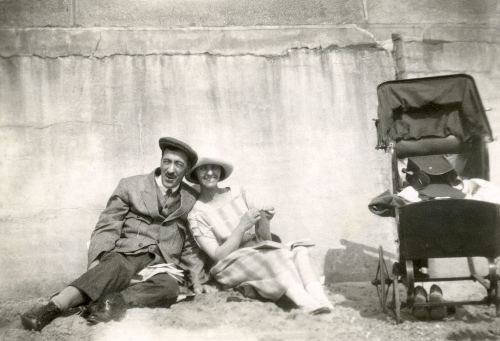 A young couple photographed in the 1920s, sitting on the sand beside a pram