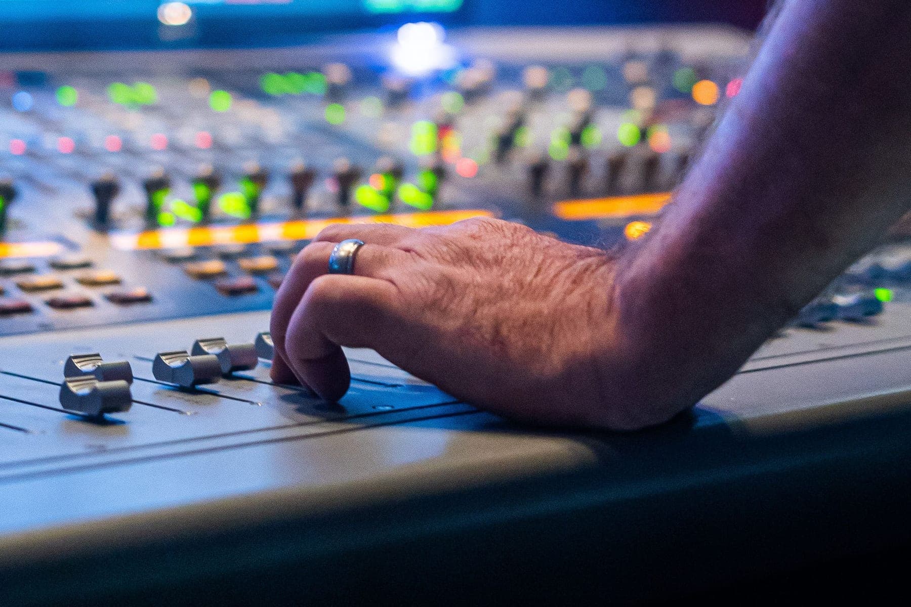 A hand resting on the faders of a large mixing desk