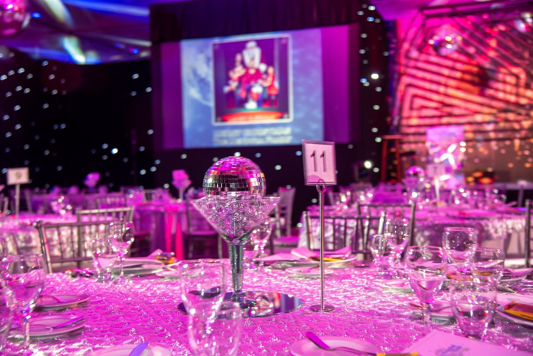 A charity gala table under pink lights, a mirror ball resting in an oversized cocktail glass at its centre