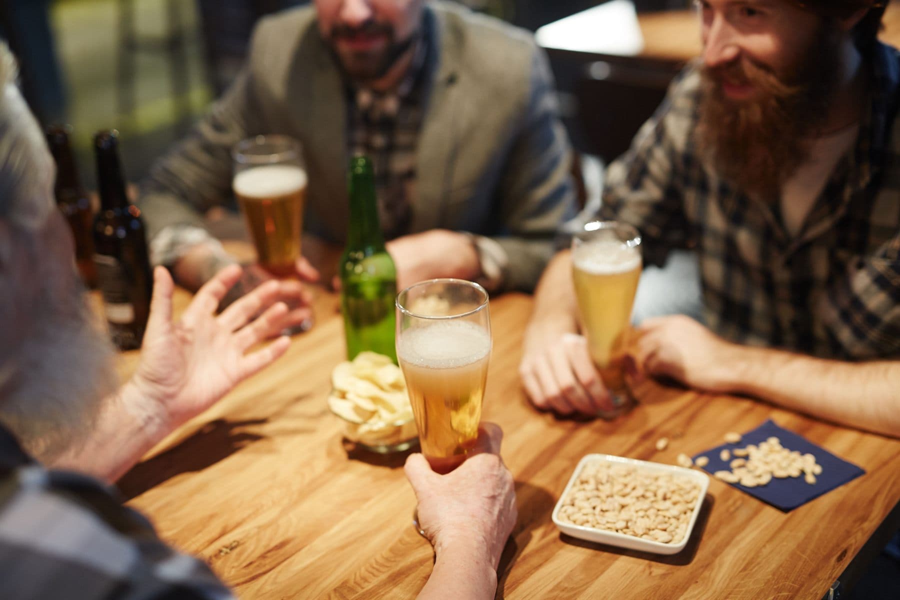 Friends around a wooden pub table, glasses of beer and a bowl of nuts between them