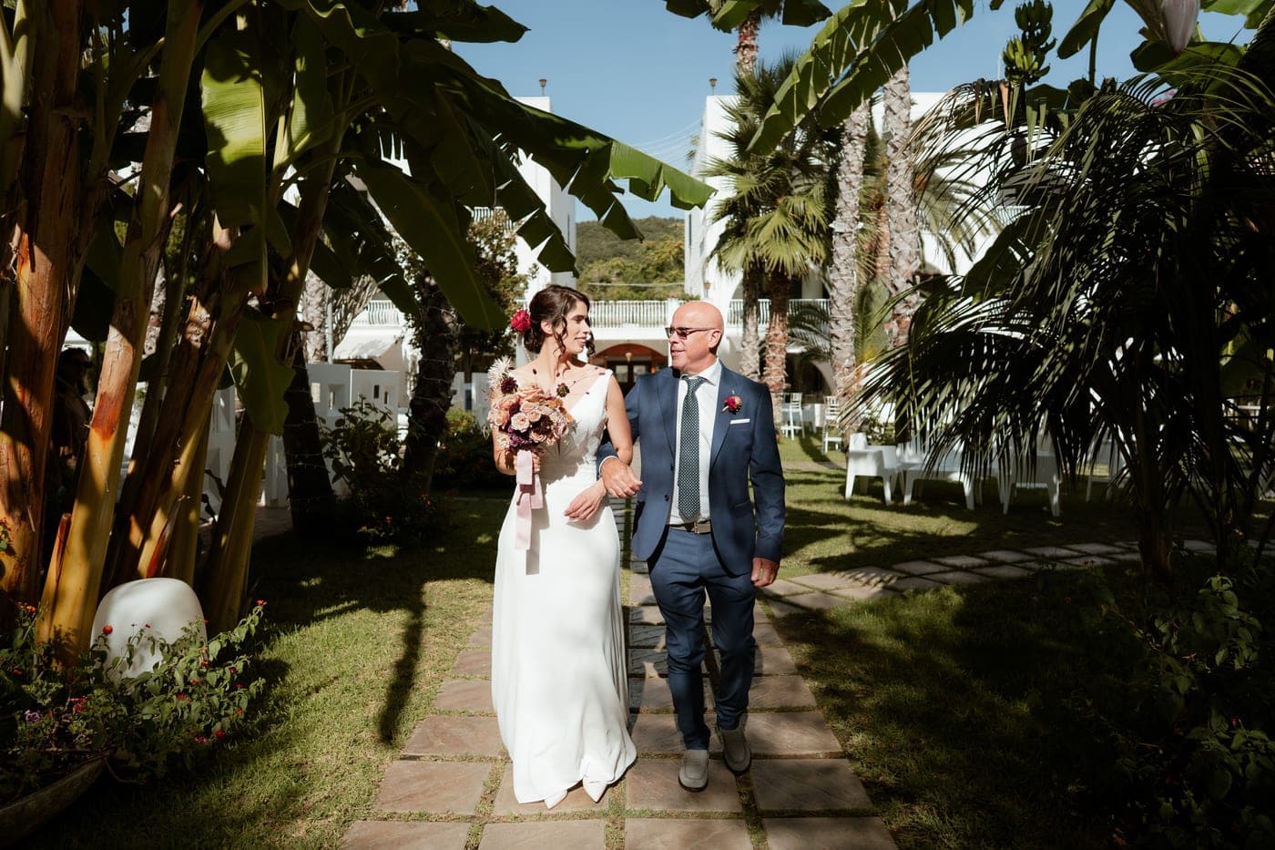 A bride walking with her father through a sunlit garden