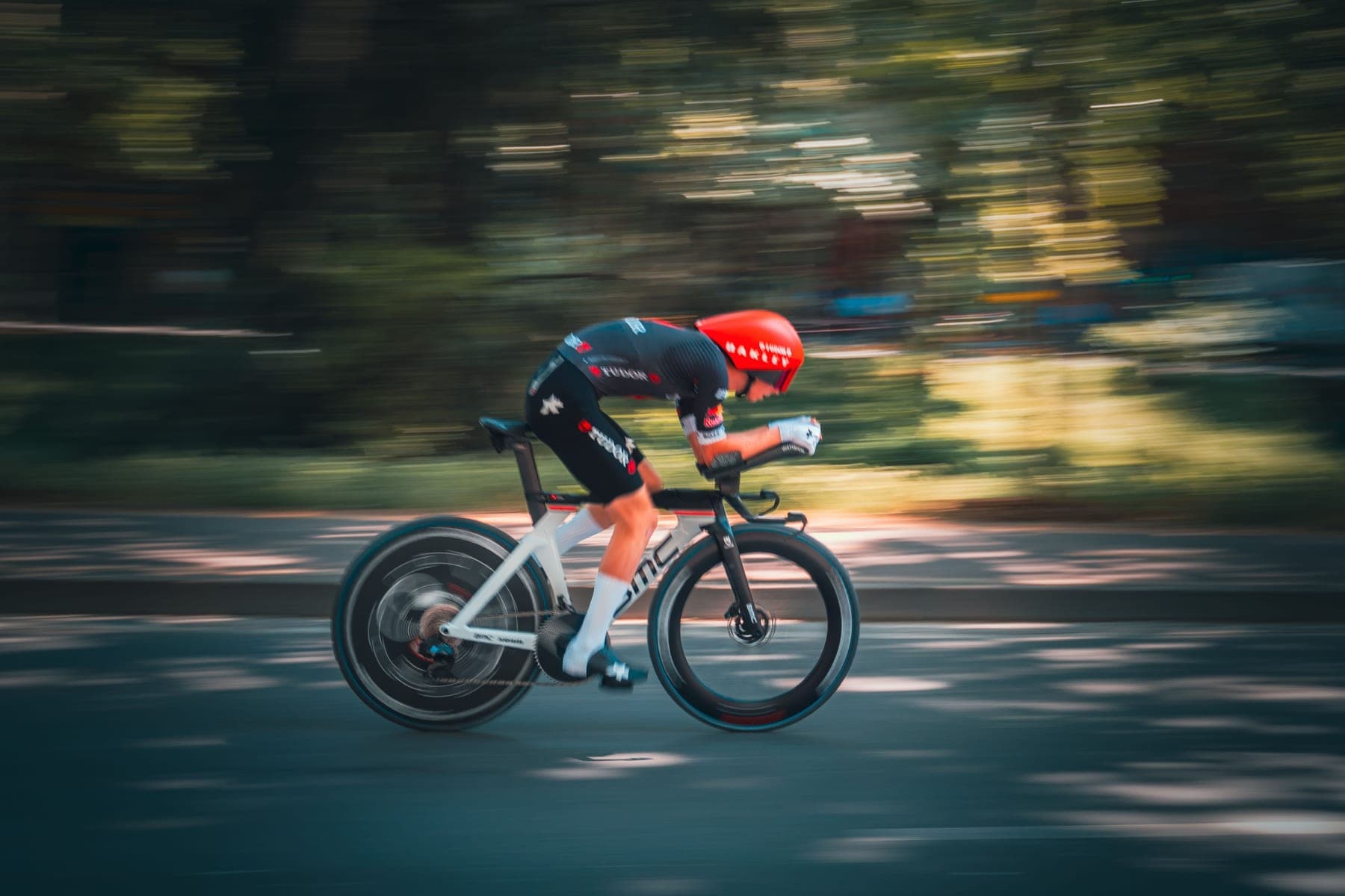 A time-trial cyclist at speed, the road and trees blurred by the panning camera