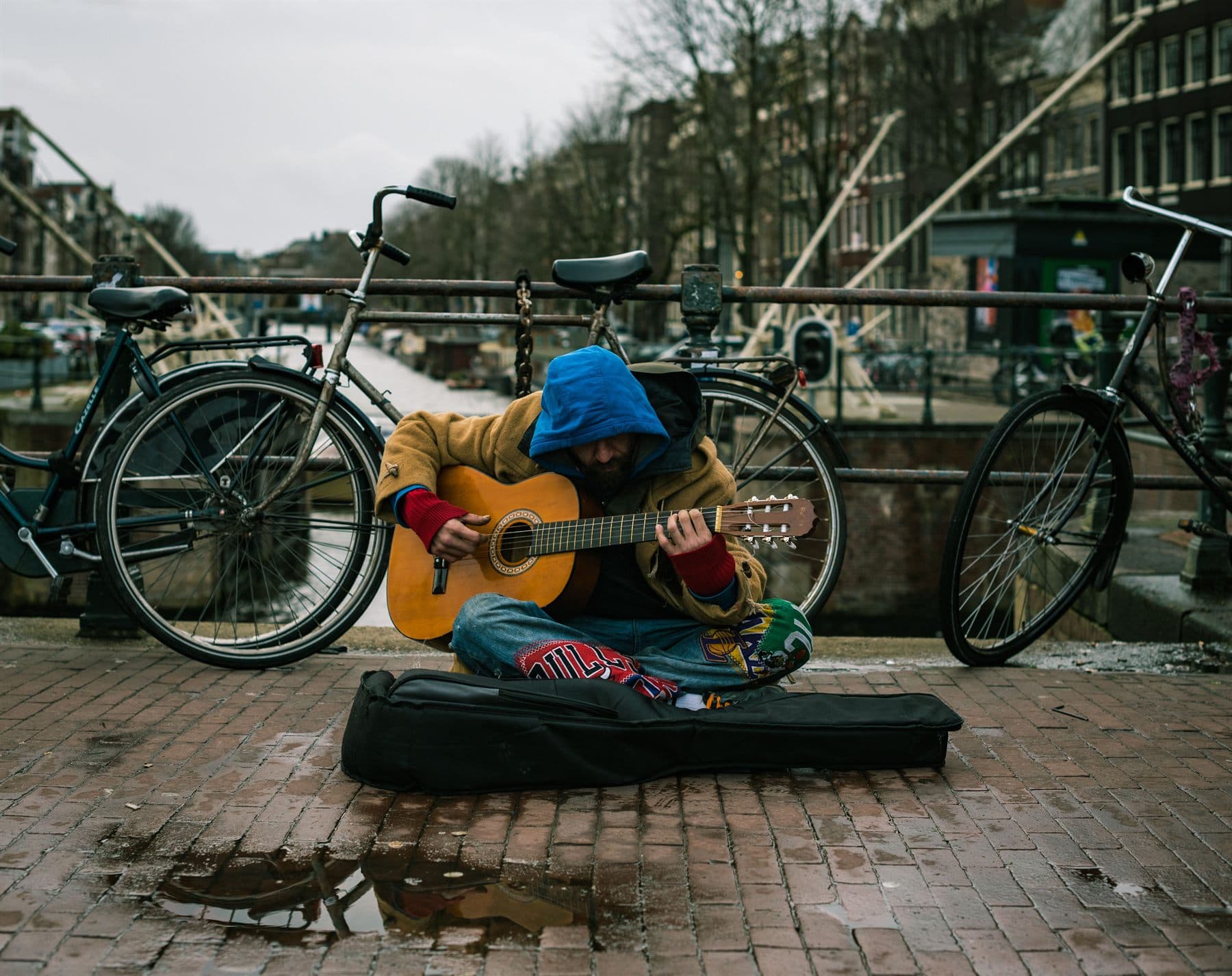 A guitarist playing an acoustic guitar on a canal bridge, bicycles leaning against the railing behind