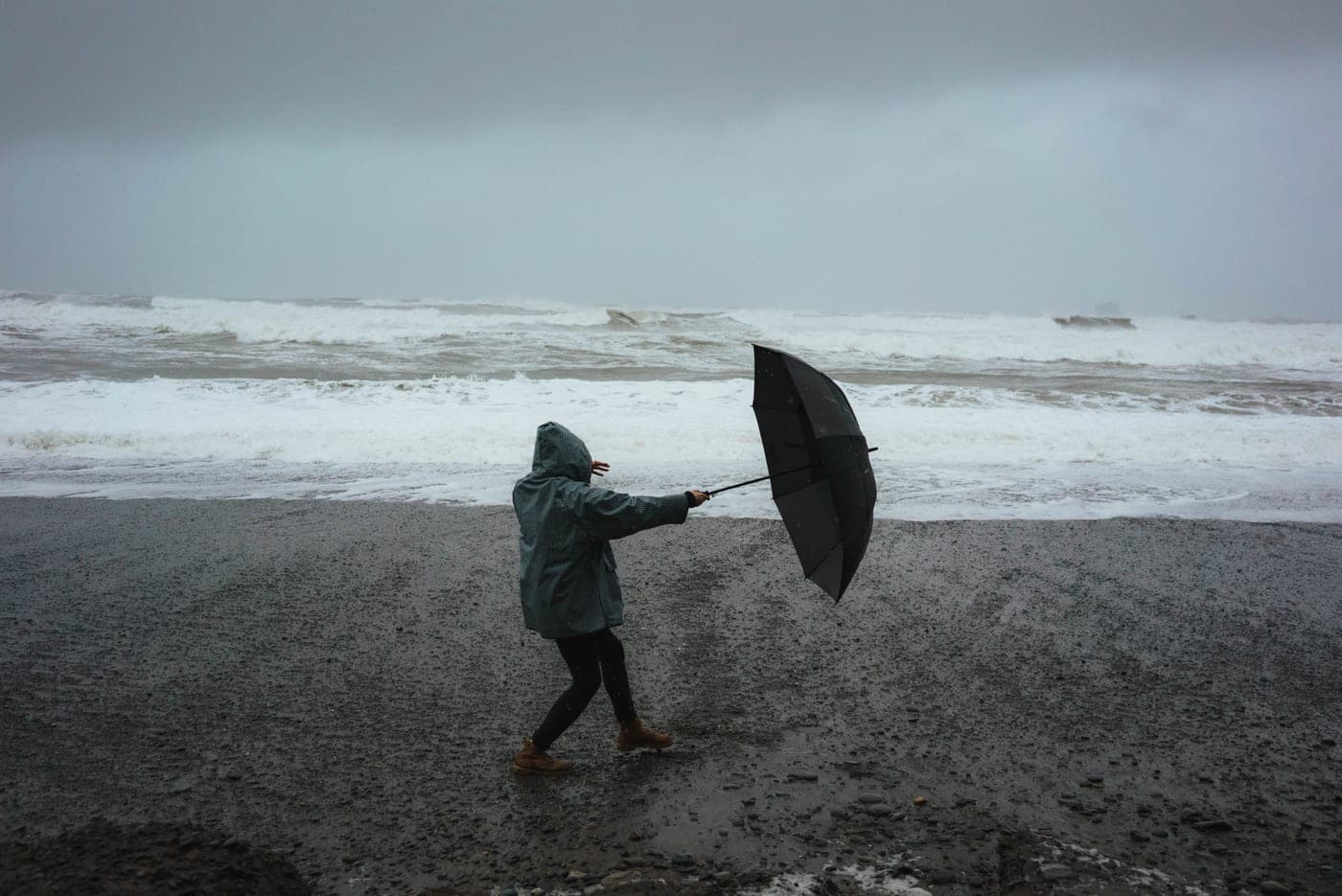 A figure on a stormy beach, umbrella turned by the wind